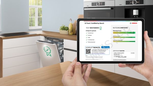 H&auml;nde halten ein Tablet mit Bosch Q‑Trust‑Zertifikat vor ge&ouml;ffneter Sp&uuml;lmaschine in einer modernen K&uuml;che.