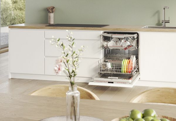 Lavastoviglie da incasso aperta con stoviglie sistemate nei cestelli, integrata in una cucina moderna con mobili bianchi 