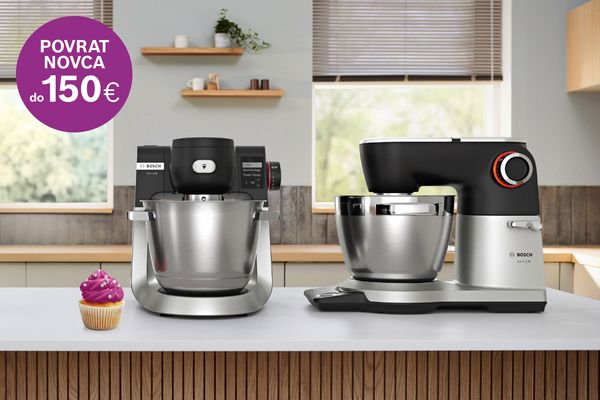 Osoba demonstrira Bosch kuhinjski mikser na drvenoj radnoj ploči, okružena staklenim posuđem i kruhom