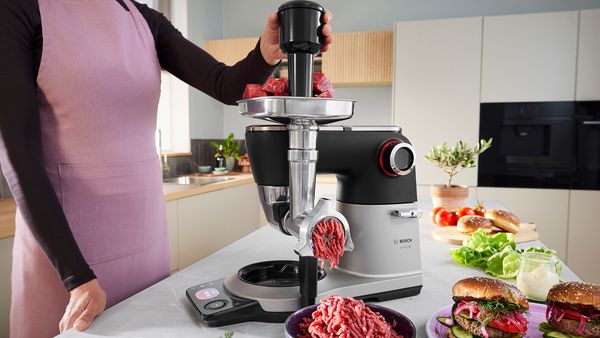 Die Serie 8 K&uuml;chenmaschine steht auf einer K&uuml;chenarbeitsplatte, w&auml;hrend eine Person den Fleischwolf an der Maschine verwendet, um Hackfleisch herzustellen.