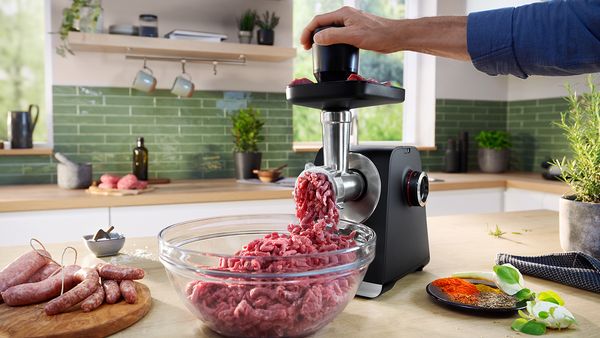 MultiPower Serie 6 mit Fleisch in der oberen Schale auf einer K&uuml;chenarbeitsplatte, daneben eine Sch&uuml;ssel mit Hackfleisch und fertige W&uuml;rstchen.