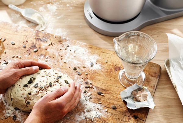 ידיים של אדם מונחות על בצק לצד מיקסר של בוש