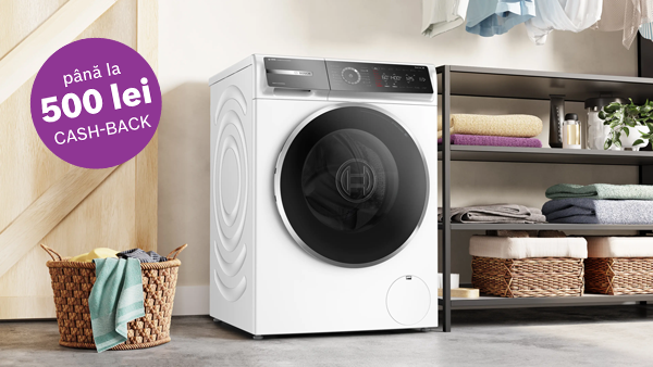 Mașină de spălat rufe intr-o incapere luminoasa alaturi de rufe curate impaturite