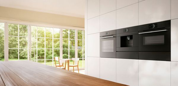 Nowoczesna kuchnia z wbudowanym czarnym podw&oacute;jnym piekarnikiem obok przytulnego salonu z sofą.