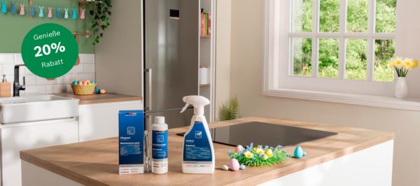 Helle K&uuml;cheninsel mit blauen Putzflaschen und Spray, Induktionsfeld, Ostereiern, Kranz, Sp&uuml;le, Fenster mit Narzissen