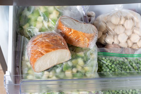 Cassetto del congelatore aperto con alimenti conservati in sacchetti, tra cui pane, broccoli, piselli e gnocchi