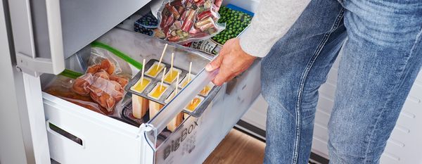 Persona che apre il cassetto del congelatore e sistema sacchetti di alimenti congelati