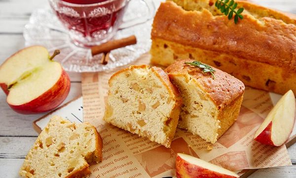 Torta di mele tagliata a fette, con mele fresche e una bevanda sullo sfondo