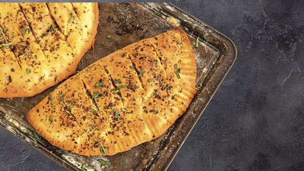 Two golden-brown calzones or garlic breads, sprinkled with herbs and spices, on a rustic baking tray.