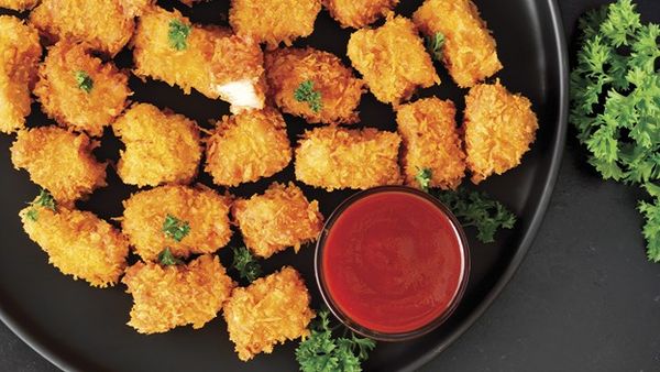 Crispy golden chicken nuggets on a black plate with a cup of ketchup and parsley garnish