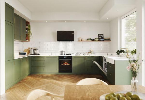 Modernt k&ouml;k med gr&ouml;na sk&aring;p, vit st&auml;nkskydd i tunnelbana, inbyggd ugn, tr&auml;golv och stort f&ouml;nster som sl&auml;pper in naturligt ljus.