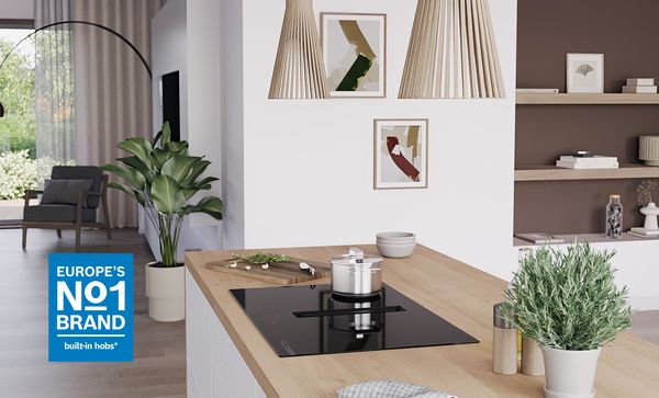 Moderna isola cucina con piano cottura a induzione incorporato, pentola, erbe fresche, piante decorative e arte murale astratta in uno spazio luminoso e accogliente.