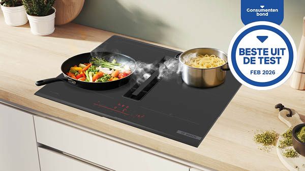 Zwart inductiekookplaat met afzuiging op houten keukentafel met potplant en andere keukenartikelen.