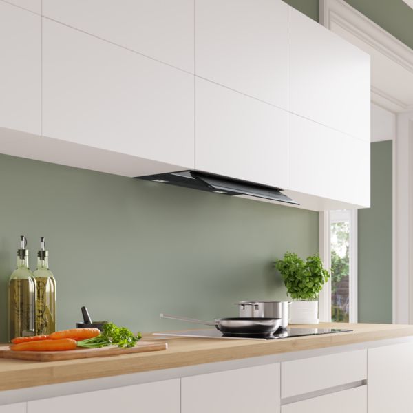 Une hotte t&eacute;lescopique noire int&eacute;gr&eacute;e sous des placards hauts blancs dans une cuisine moderne avec un plan de travail en bois et un mur vert sauge.