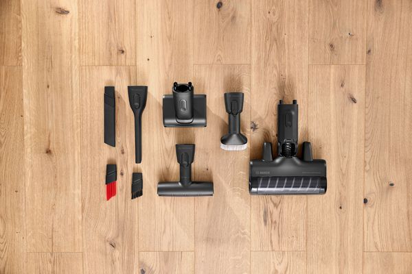 Accessori per aspirapolvere Bosch disposti su pavimento in legno: bocchette, spazzole e testine