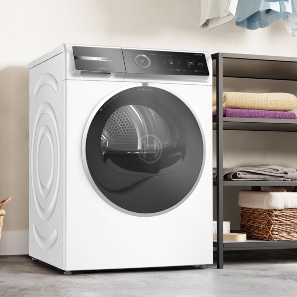 Un s&egrave;che-linge blanc de Bosch est plac&eacute; dans une buanderie, &agrave; c&ocirc;t&eacute; d'une &eacute;tag&egrave;re sombre avec des serviettes pli&eacute;es.