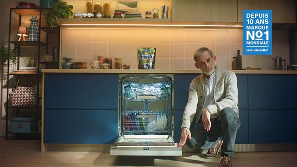 Un homme est accroupi &agrave; c&ocirc;t&eacute; d'un lave-vaisselle ouvert rempli de vaisselle propre dans une cuisine moderne.