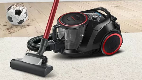 Schwarz-roter Staubsauger auf einem wei&szlig;en Teppich in der N&auml;he eines Holzbodens mit einem schmutzigen Fu&szlig;ball.