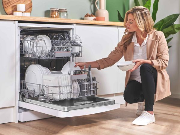 Person taking clean dishes out of full dishwasher