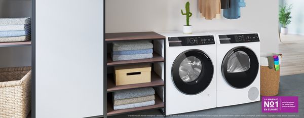 Un lave-linge et un s&egrave;che-linge se trouvent entre des &eacute;tag&egrave;res et un panier &agrave; linge dans une pi&egrave;ce joyeuse.