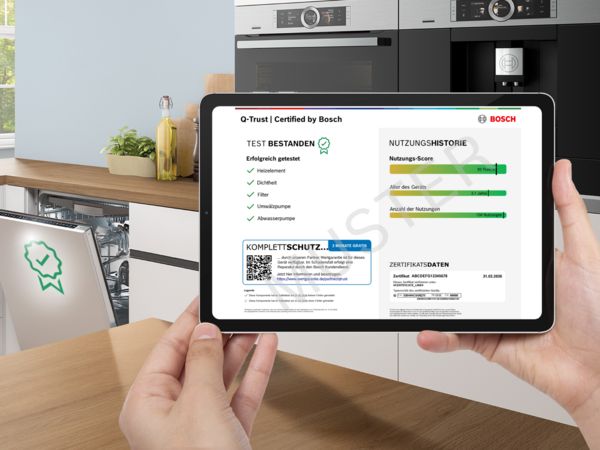 Hand h&auml;lt Tablet mit Bosch‑Zertifikat vor offenem Geschirrsp&uuml;ler in moderner K&uuml;che.