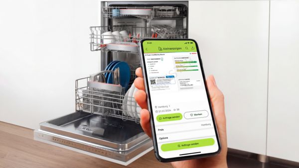 Hand h&auml;lt Smartphone mit Kleinanzeigen-App und Bosch Q-Trust Zertifikat vor offenem, beladenem Geschirrsp&uuml;ler.