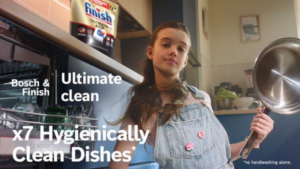 Child holding clean pan next to open dishwasher with Finish pack above
