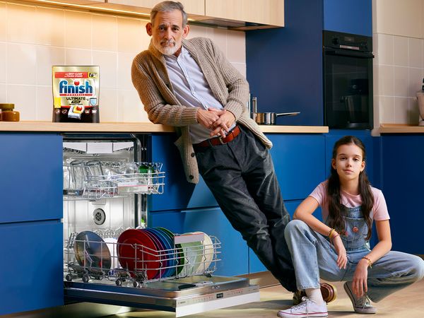 Adult and child next to open dishwasher with Finish pack above on countertop