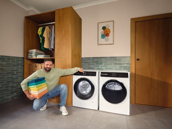 Man met krullend haar naast wasmachine in wasruimte.