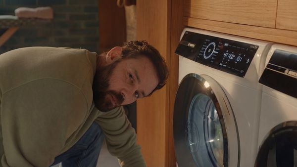 Man kijkt naar de camera met de op achtergrond een Bosch wasmachine, gemaakt om lang mee te gaan.