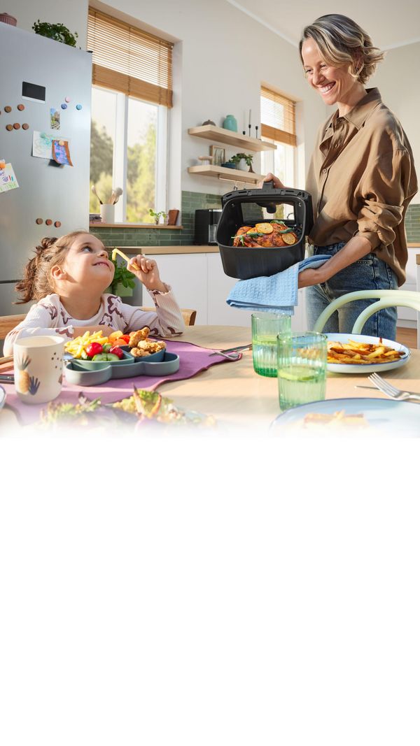 Kobieta i dziecko w kuchni air fryer na blacie w kuchni, obok potrawy na talerzach