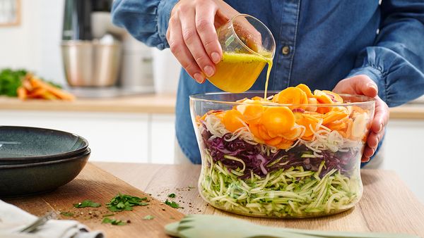 Mit der K&uuml;chenmaschine geraspeltes Gem&uuml;se wird zu einem bunten Rohkostsalat verarbeitet und mit Dressing abgeschmeckt.