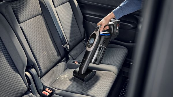 Es ist die Hand einer Person zu sehen, die mit dem Handteil des Unlimited 10 Akku-Staubsaugers von Bosch mit Mini-Turbo-D&uuml;se einen Autositz absaugt.
