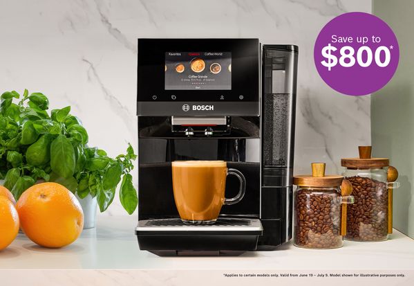 Bosch coffee machine brewing a latte with oranges, basil plant, and jars of coffee beans on a kitchen counter.