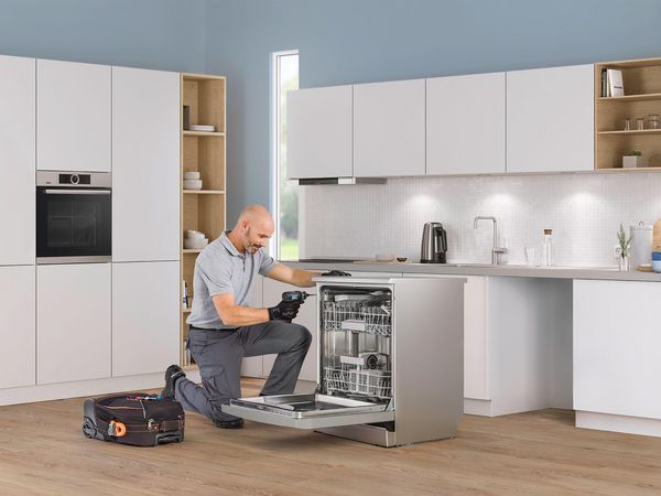 Toolbox and tablet symbolising the repair hotline on a kitchen table with a Bosch refrigerator in the background. 