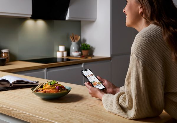 Donna che utilizza l'app Home Connect sullo smartphone per gestire gli elettrodomestici smart Bosch in cucina