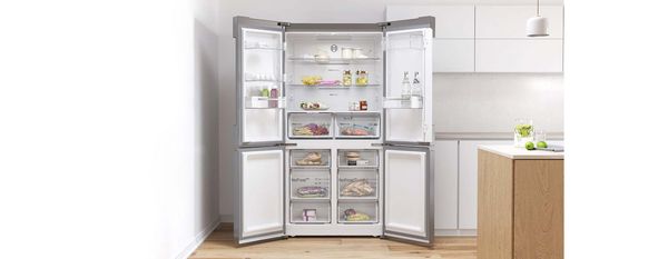 Un moderno frigorifero a quattro porte aperto in una cucina luminosa, mostrando scaffali organizzati con cibo e bevande all'interno.