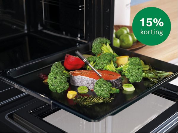 Siemens kookplaat met daarop een grillplaat met lamskoteletjes en tomaat. Aan zijkant olie en houtenplank