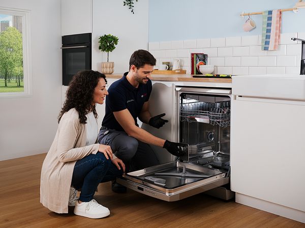 Serwisant naprawia otwarta zmywarke, przy nim jest kobieta