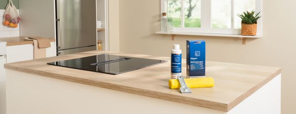 Piano cottura a induzione Bosch su un'isola da cucina con prodotti Cleaning&Care e panno in microfibra per la pulizia