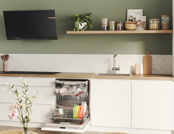 Open Bosch vaatwasser ingebouwd in moderne witte keuken met zwarte afzuigkap en houten werkblad.