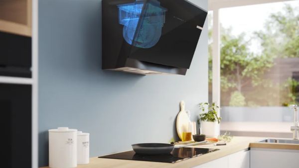 Bosch zwarte schuine afzuigkap met blauw digitaal display, gemonteerd in moderne keuken boven inductiekookplaat met pan.  