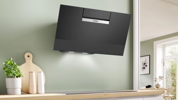 Bosch zwarte schuine wandafzuigkap gemonteerd op groene muur boven houten aanrecht in lichte keuken.    