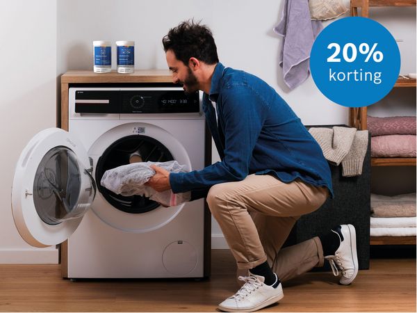 Man die voor de wasmachine zit, met reinigingsmiddelen bovenop de wasmachine in de wasruimte