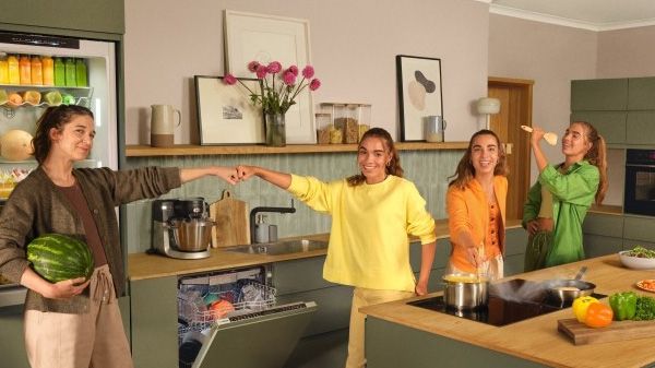 Man in keuken koken, houden van een schotel, omgeven door kleurrijke keukengerei en apparatuur.