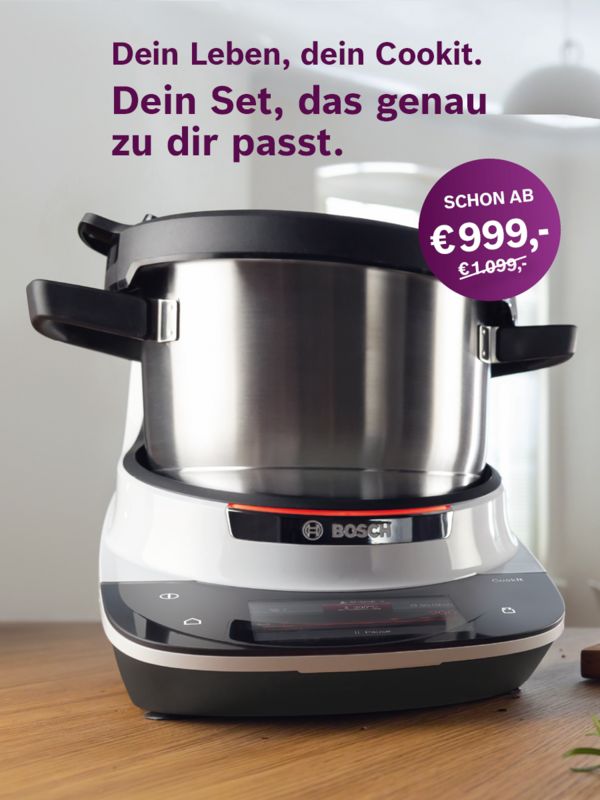Eine Frau steht mittig in der K&uuml;che an einem Schneidebrett und bereitet Essen zu.