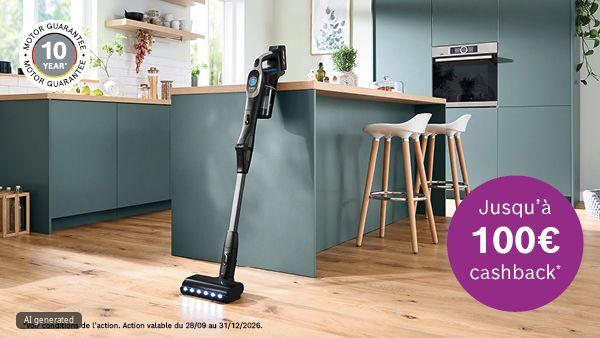 Aspirateur-balai pos&eacute; sur un sol en bois devant un &icirc;lot de cuisine aux meubles vert-bleu et des tabourets ; des LED sur la brosse &eacute;clairent le sol. En haut &agrave; gauche, un badge rond libell&eacute; &laquo;10 year motor guarantee&raquo;, en bas &agrave; droite un cercle violet indiquant &laquo;Jusqu'&agrave; 100&euro; cashback*&raquo;.