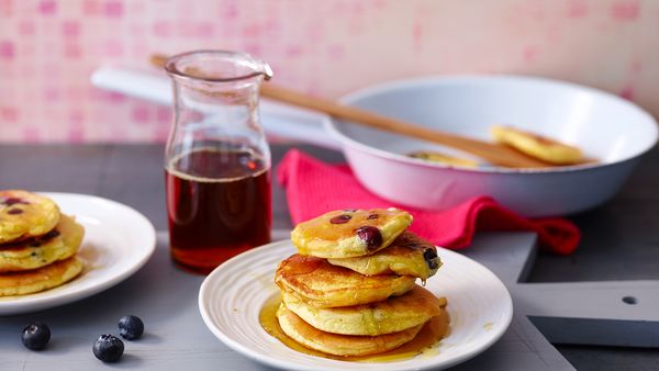 Nahaufnahme von einem Stapel goldbrauner American-Style Pancakes mit Ahornsirup und Blaubeeren auf wei&szlig;em Keramikteller.