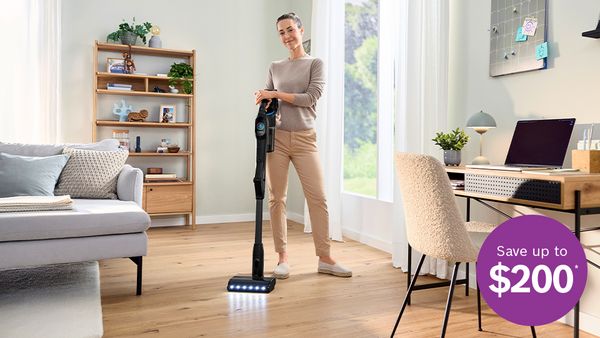 Woman using a cordless vacuum in a bright living room, with a &ldquo;Save up to $200&rdquo; promotional graphic.