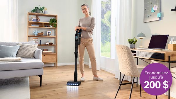 Une femme utilisant un aspirateur sans fil dans un salon lumineux, avec un visuel promotionnel indiquant &laquo; &Eacute;conomisez jusqu'&agrave; 200 $ &raquo;.